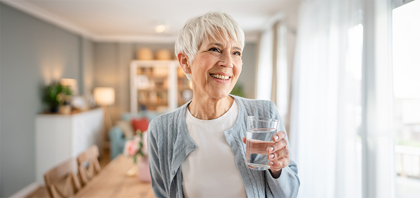 A senior woman smiling while holding a glass of water.